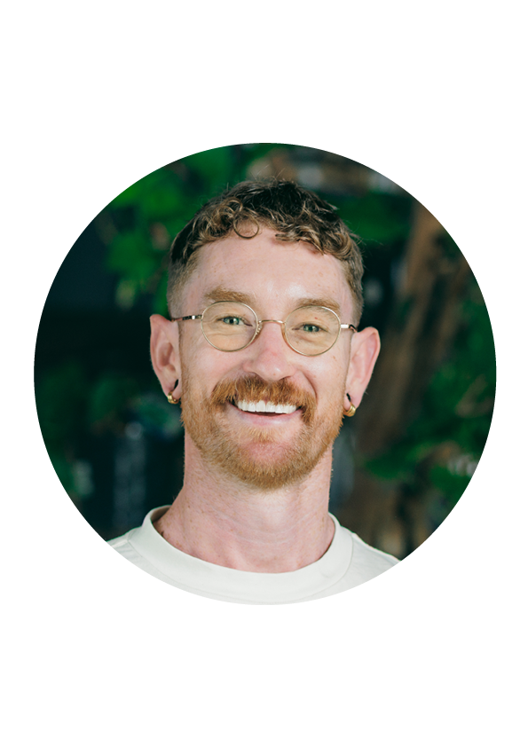 Circular portrait of a person with glasses and a beard, set against a blurred natural background.