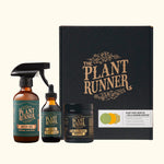 A collection of plant care products from The Plant Runner, including a bottle each of indoor plant food, neem oil leaf shine, and soil and microbes booster, packaged in a black gift box.
