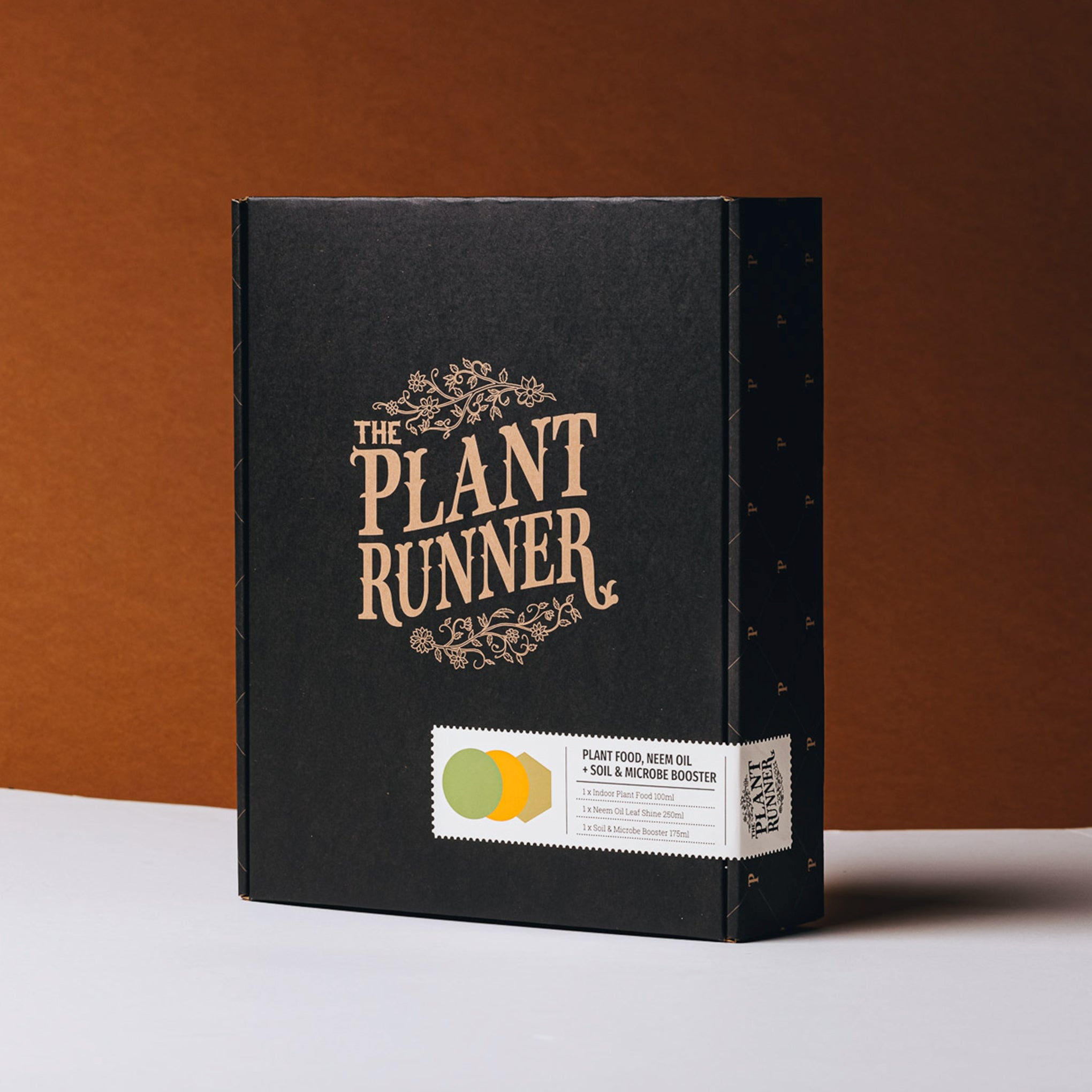 A collection of plant care products from Plant Runner including a bottle of indoor plant food, neem oil leaf shine, and a jar of soil and microbes booster, packaged in a black gift box with the Plant Runner logo.